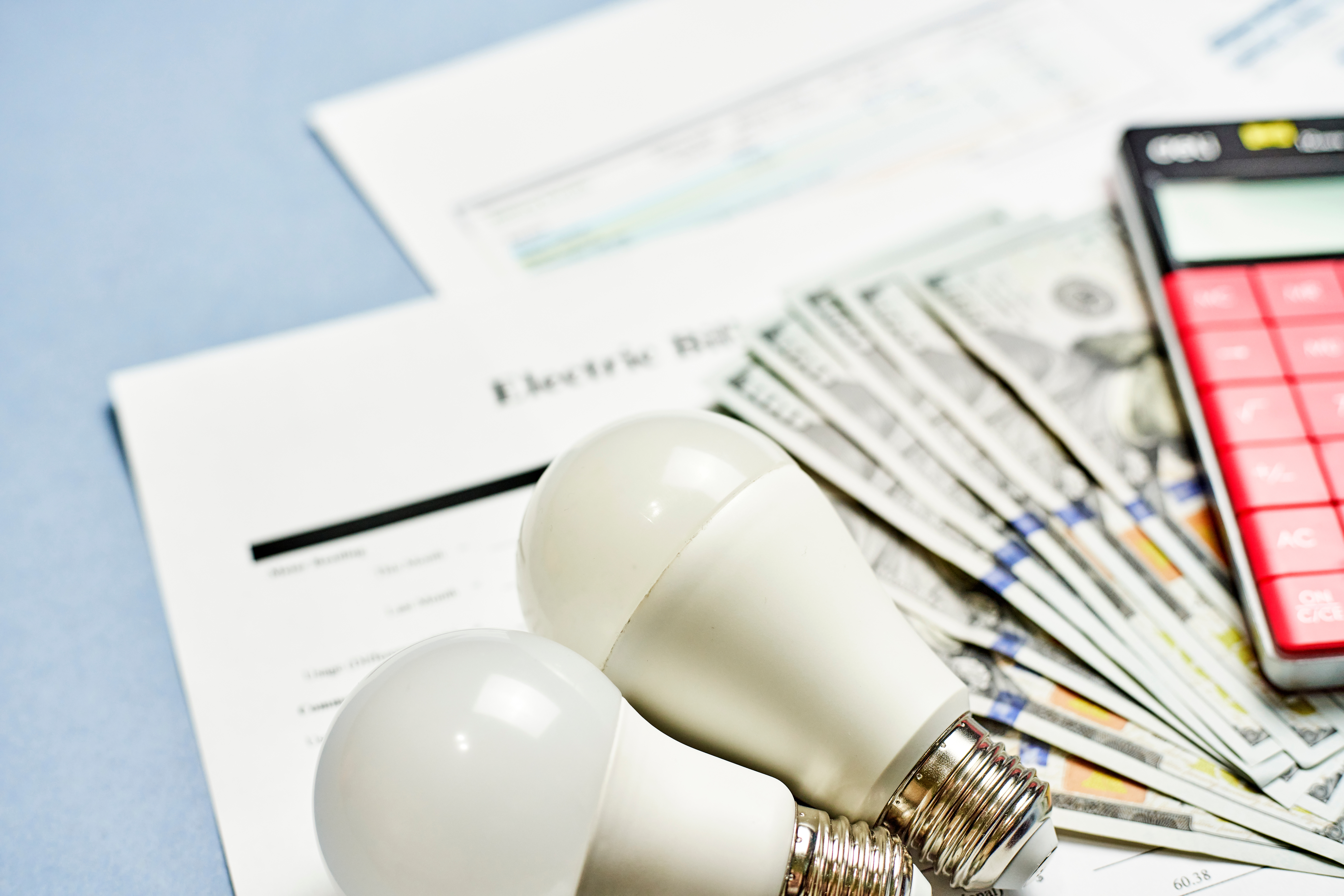 A utility bill with light bulbs and money on top - learn how to lower your electric bill with Custom Electrical Services .