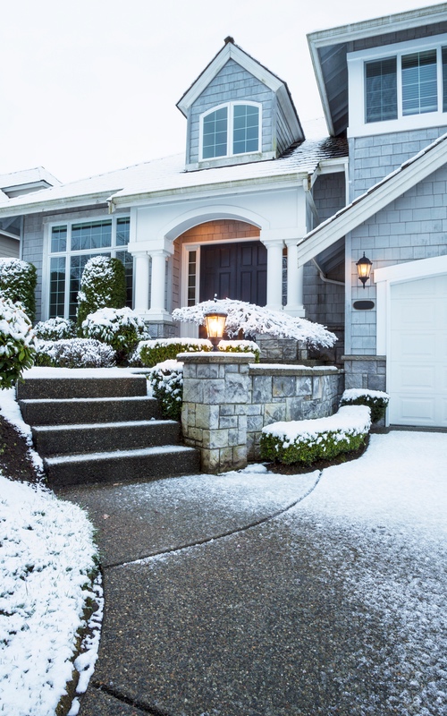 A light blue home with a snow-covered yard, learn how to avoid electrical hazards in the winter with Custom Electrical Services .